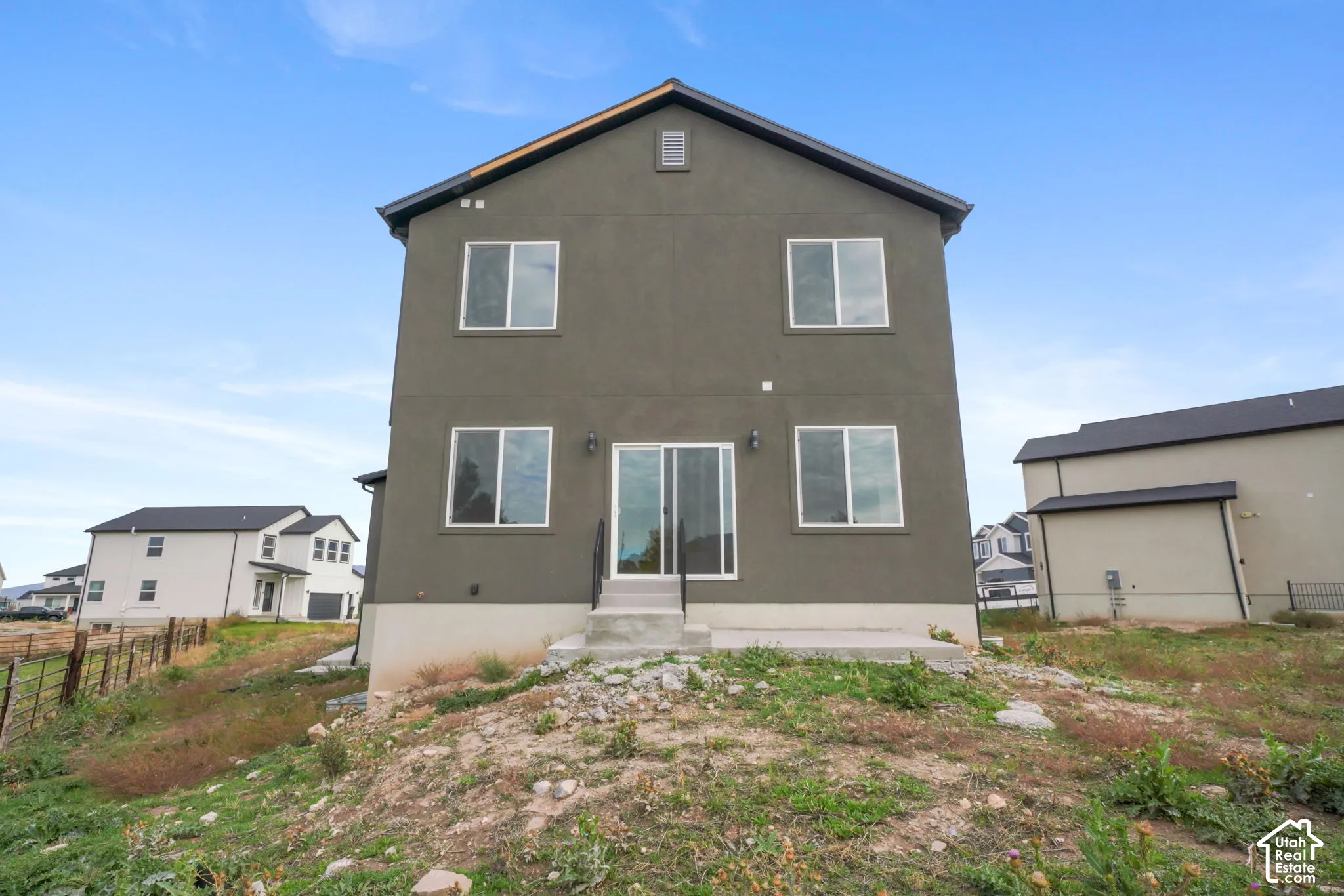Two-story exterior featuring a dark stucco facade, gabled roofline, sliding glass patio door, and a concrete rear landing with metal handrails