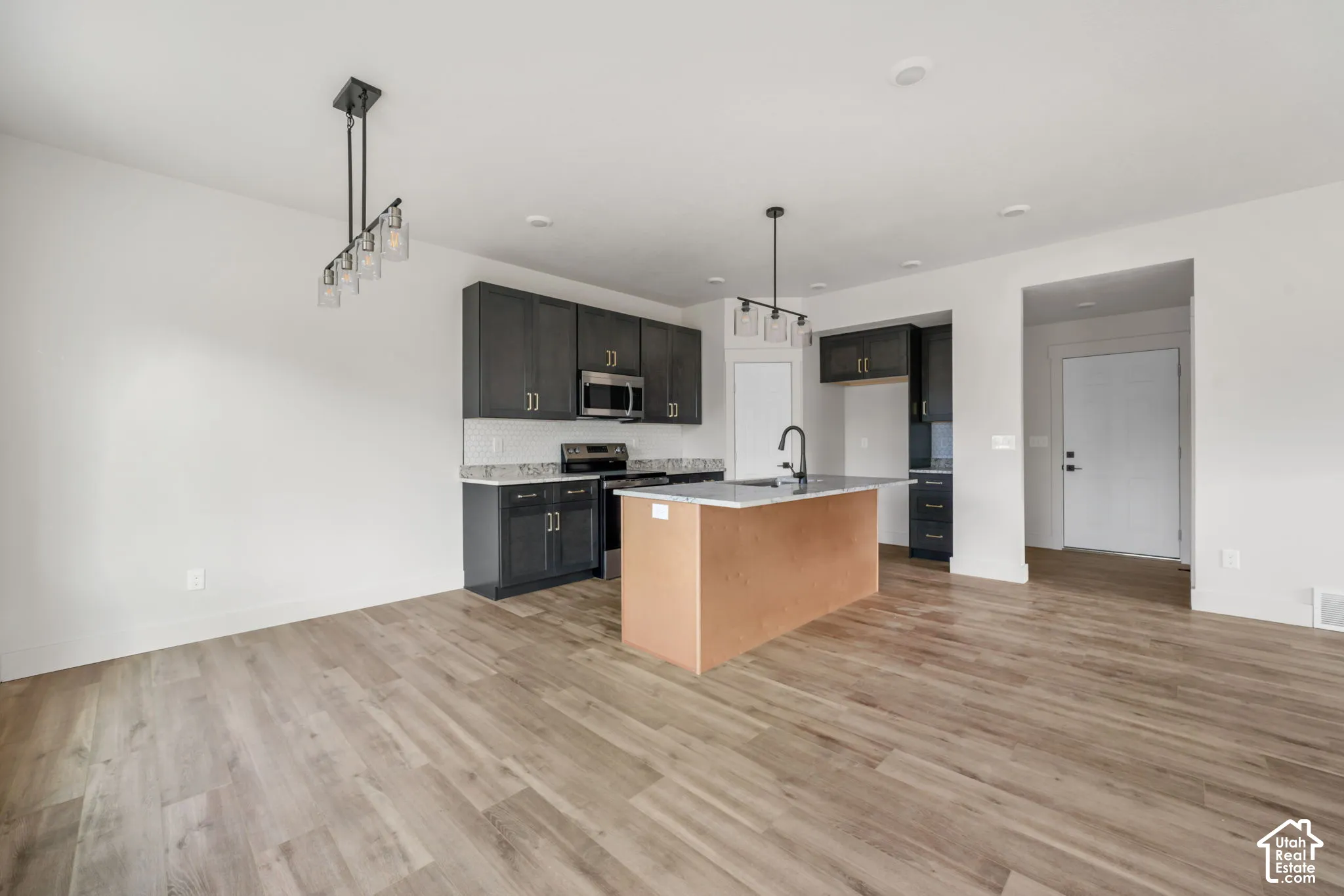 Kitchen featuring dark cabinetry, stone-finish countertops, a central island with an integrated sink, and wood-finish flooring