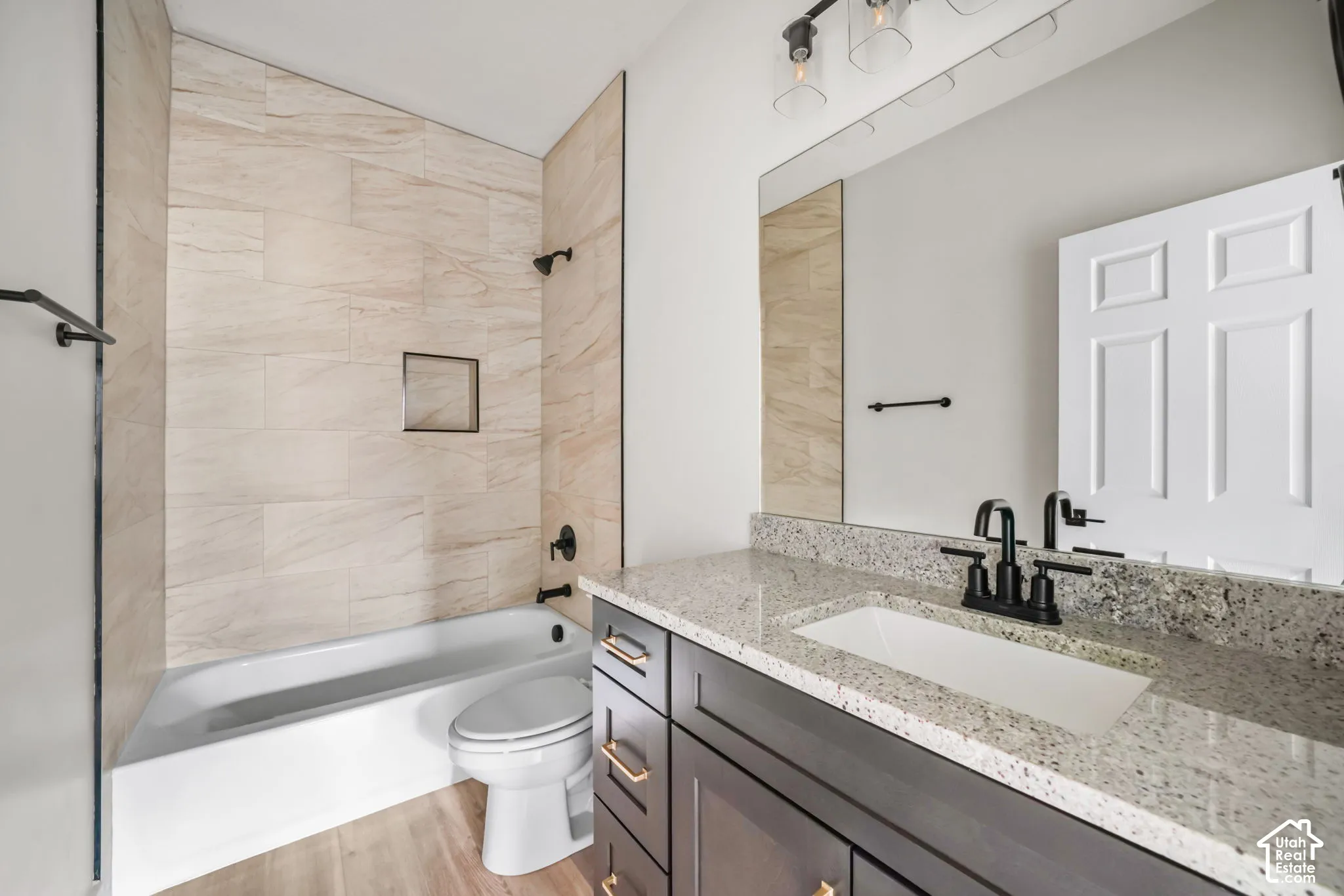 Bathroom featuring a vanity with stone-finish countertop, undermount sink, matte black faucet hardware, and a tub-shower combination with floor-to-ceiling tile surround and built-in recessed shelving
