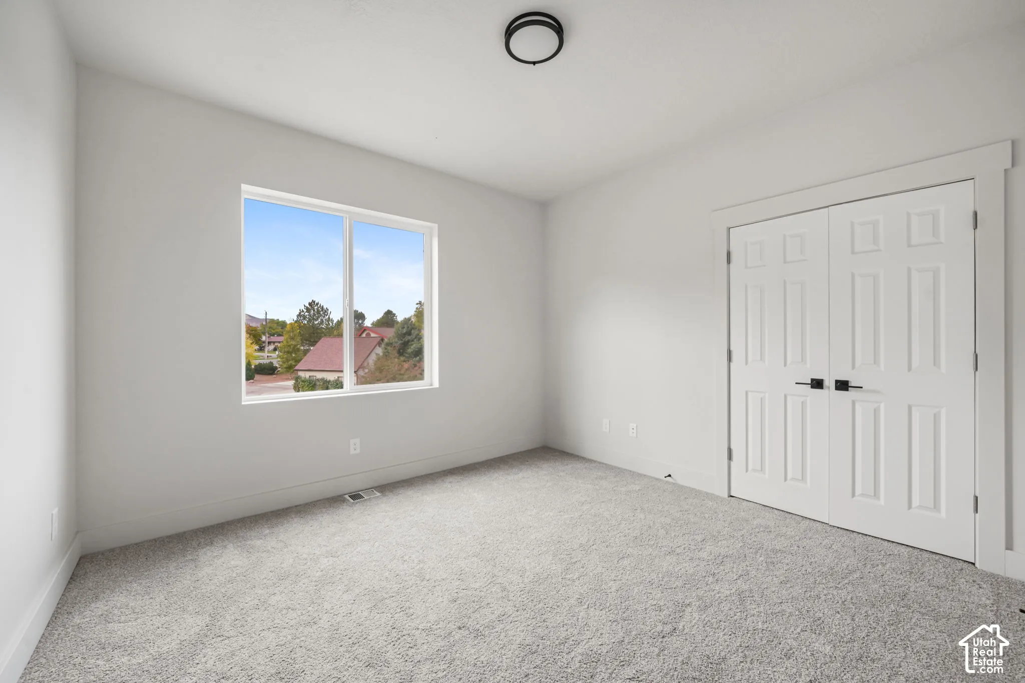 Neutral-toned carpeted flooring, double-panel closet doors with matte black hardware, and an expansive window with exterior landscape exposure