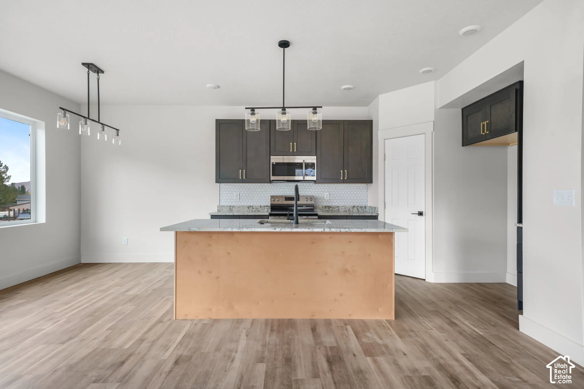 Kitchen featuring dark-finish cabinetry, stone-patterned countertops, a central island, hexagonal tile backsplash, and wood-finish flooring