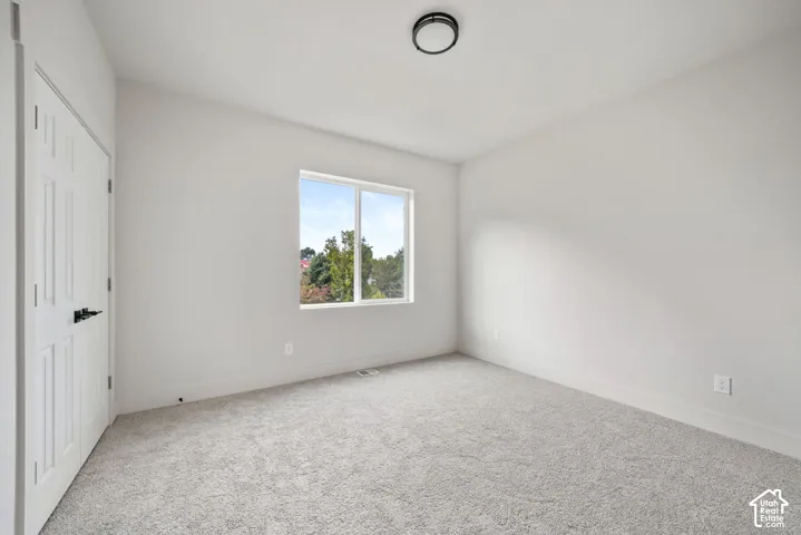 Neutral-toned wall paint, plush carpeting, single-pane window, and a double-door closet featuring matte black hardware