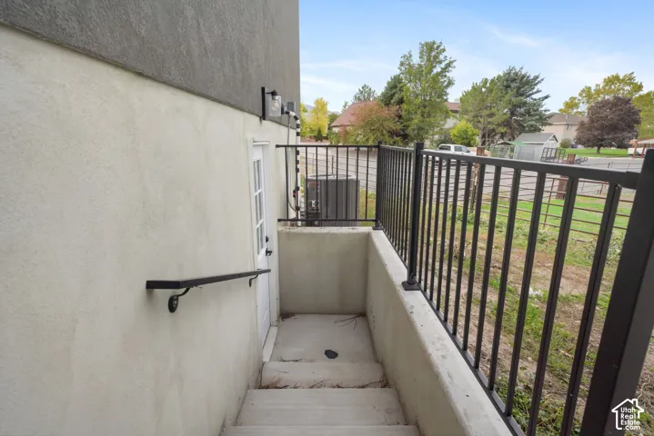 Exterior staircase featuring concrete steps, smooth stucco siding, metal handrail, and black metal perimeter fencing