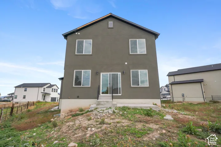 Two-story exterior featuring a dark stucco facade, gabled roofline, sliding glass patio door, and a concrete rear landing with metal handrails