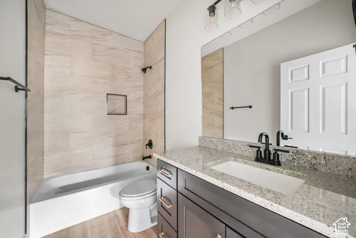 Bathroom featuring a vanity with stone-finish countertop, undermount sink, matte black faucet hardware, and a tub-shower combination with floor-to-ceiling tile surround and built-in recessed shelving