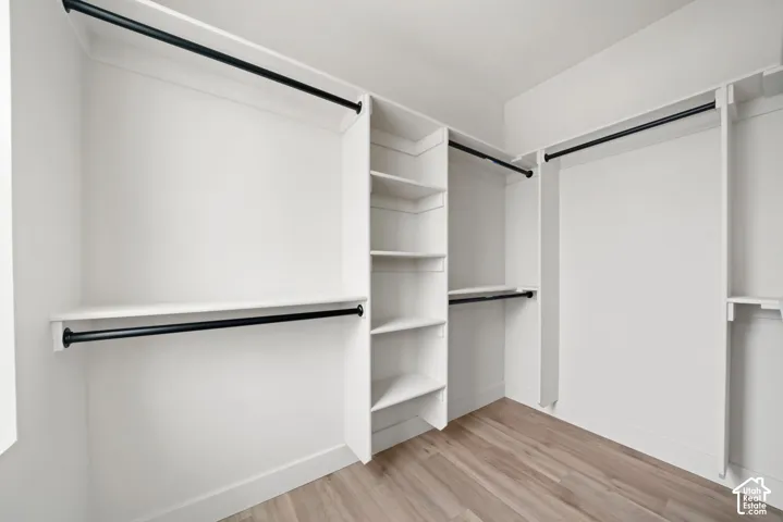 Walk-in closet featuring white built-in shelving, wood-finish flooring, and matte black hanging rods