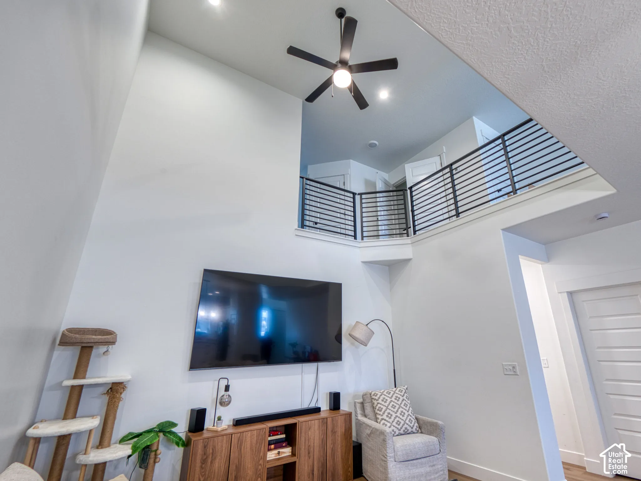 Vaulted ceilings, matte black ceiling fan with integrated lighting, and horizontal metal railing overlooking the area