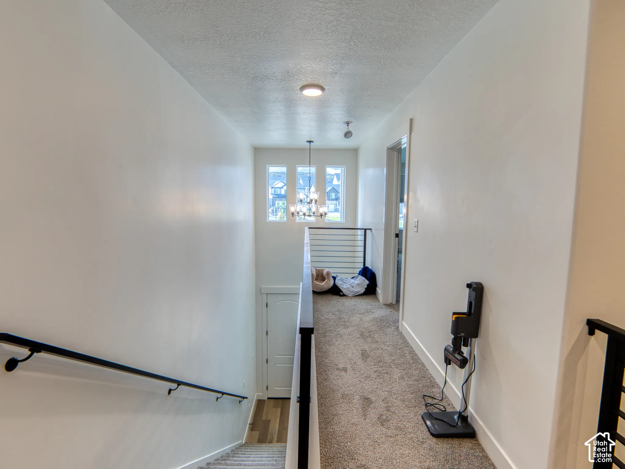 Hallway featuring a multi-light chandelier, horizontal metal stair railing, and tall windows