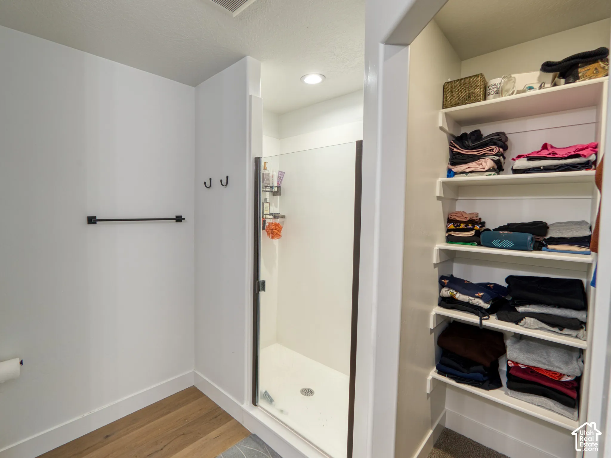 Maser bathroom, Shower stall with a glass door and frame, built-in shelving, matte black hardware, and wood-finish flooring