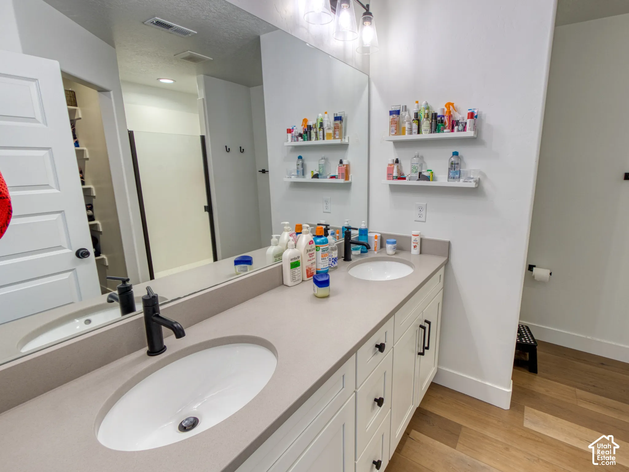 Master bathroom, Dual-vanity bathroom featuring solid-surface countertops, undermount oval sinks, matte black hardware, built-in shelving, and wood-finish flooring