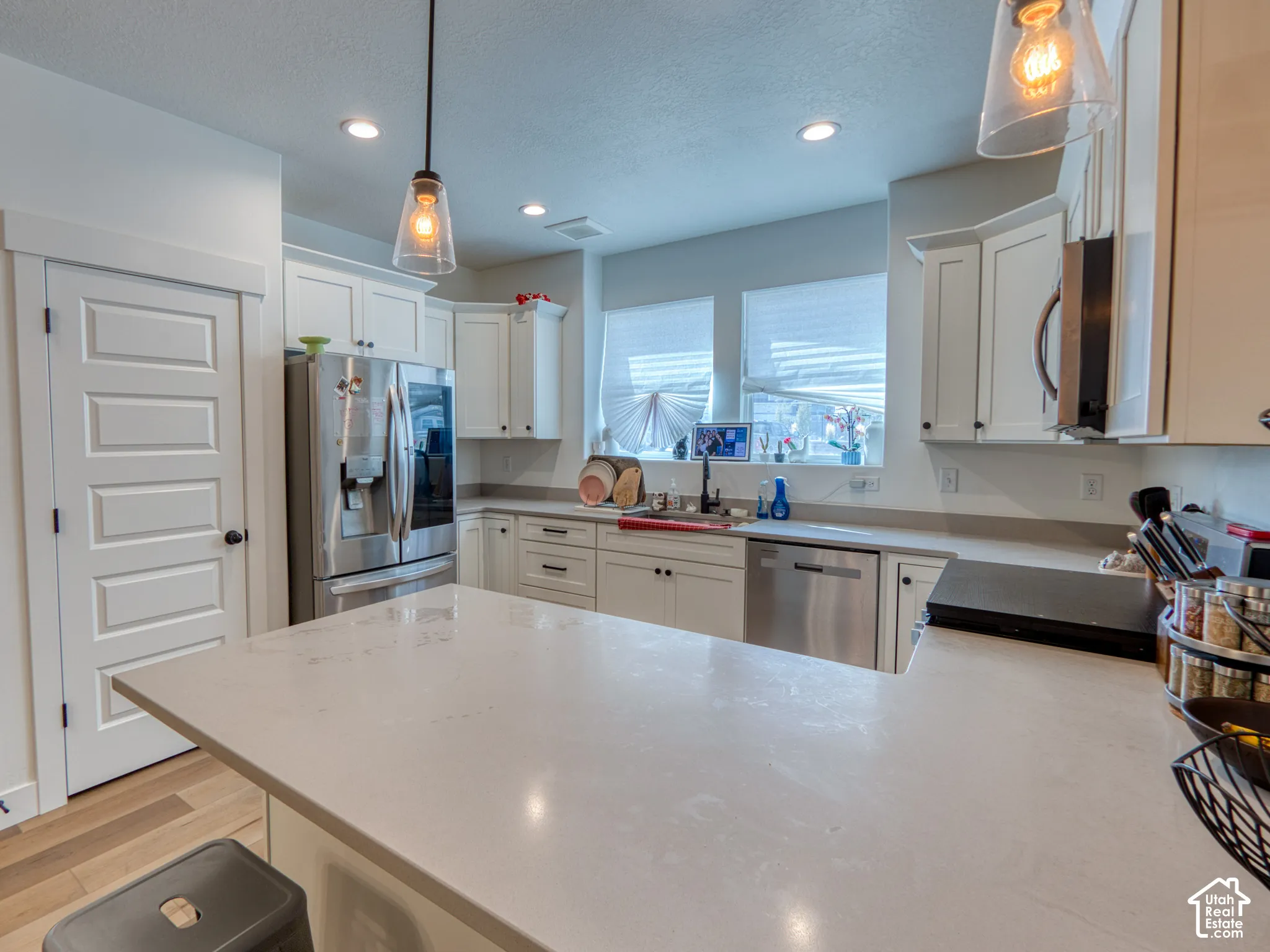 Kitchen featuring white shaker-style cabinetry, quartz countertops, stainless steel appliances, a peninsula with pendant lighting, and wood-finish flooring