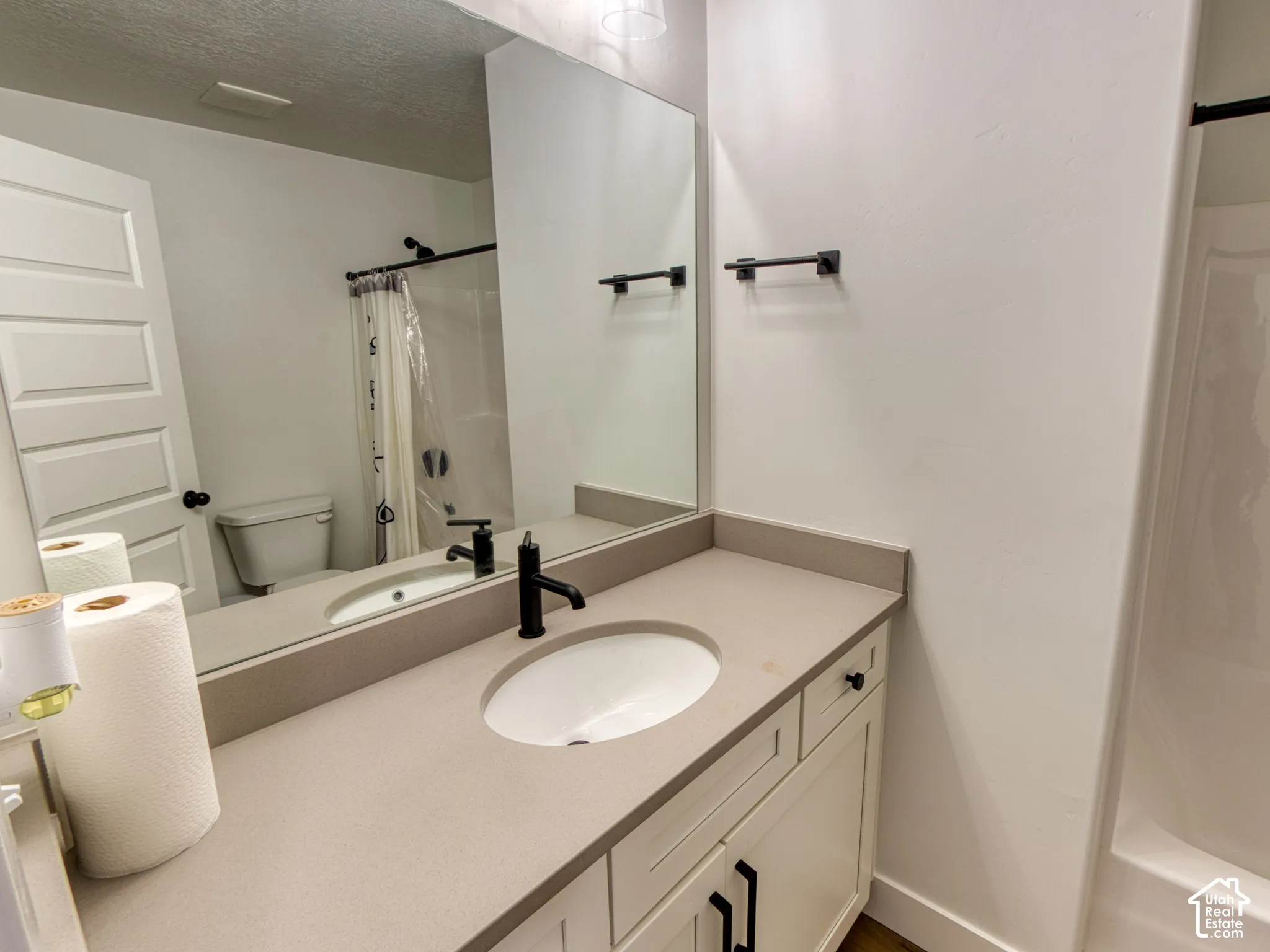 Secondary Full Bathroom featuring a stone-composite countertop with an integrated oval sink, matte black faucet and hardware, shaker-style vanity cabinetry, and a full-width vanity mirror