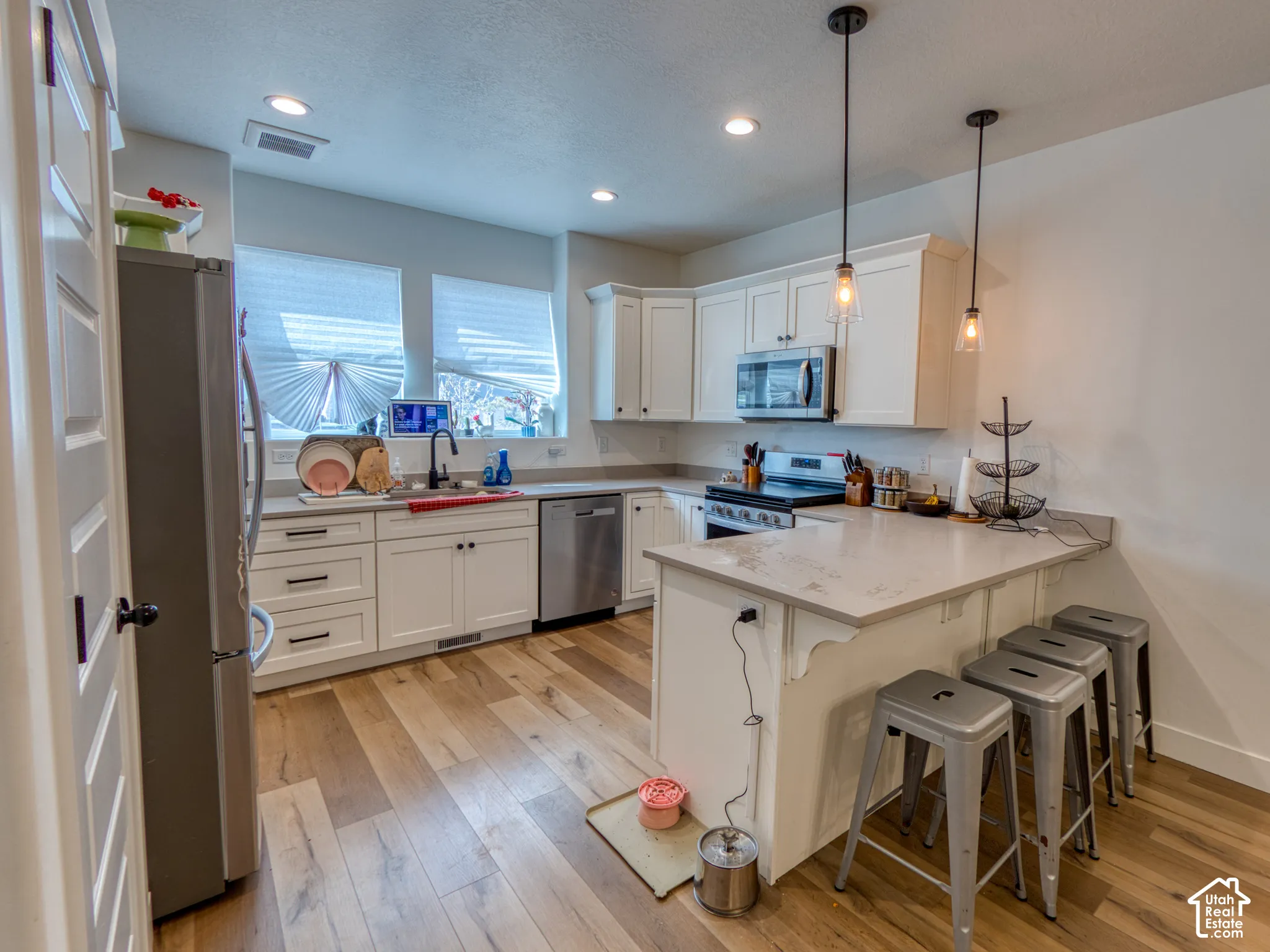 Kitchen featuring white shaker-style cabinetry, solid-surface countertops, wood-finish flooring, recessed lighting, and stainless steel appliances