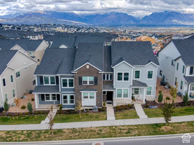 Multi-story exterior featuring a mix of horizontal siding, brick masonry, and stone veneer accents under a dark shingle roof with a backdrop of mountain scenery