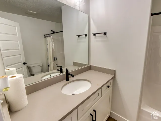 Secondary Full Bathroom featuring a stone-composite countertop with an integrated oval sink, matte black faucet and hardware, shaker-style vanity cabinetry, and a full-width vanity mirror