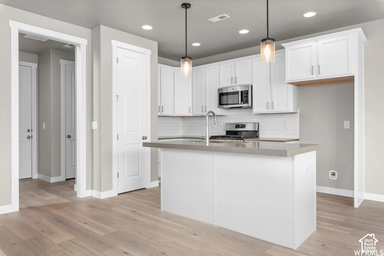 Kitchen featuring white shaker-style cabinetry, a central island with a solid-surface countertop, subway tile backsplash, stainless steel appliances, and wood-finish flooring