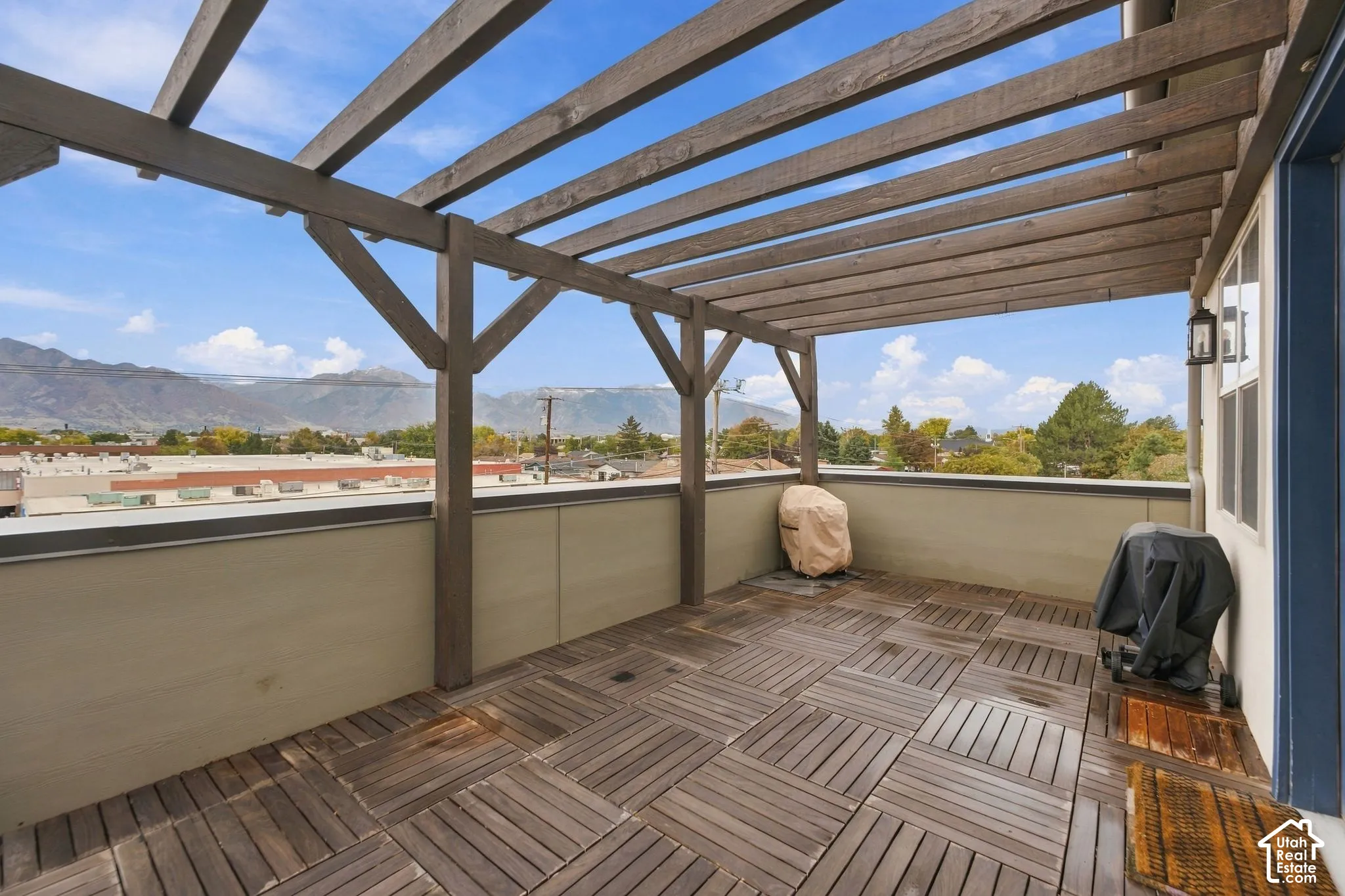 Covered rooftop deck featuring wood-finish decking tiles, an overhead timber pergola, and mountain scenery