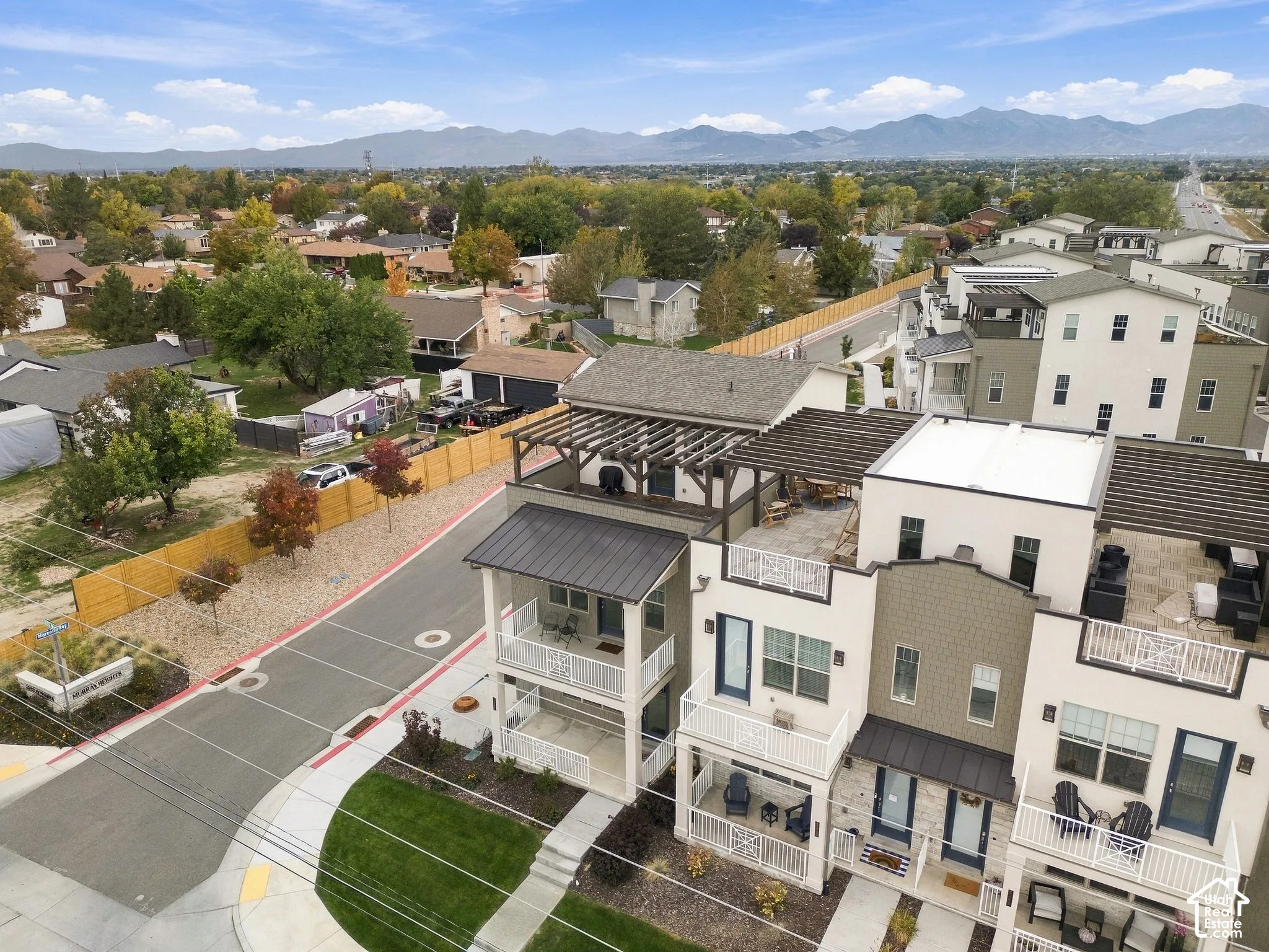 Multi-story residences featuring metal roof accents, private terraces with wooden pergolas, multi-level balconies, and a backdrop of mountain scenery