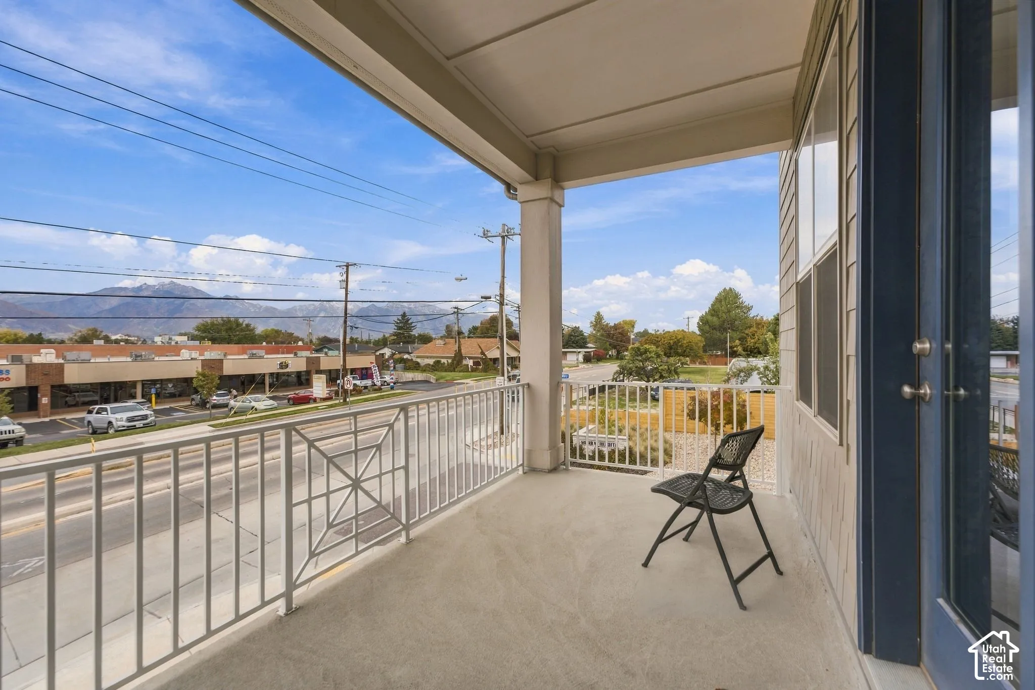 Covered outdoor balcony featuring white metal railings, concrete flooring, and mountainous scenery
