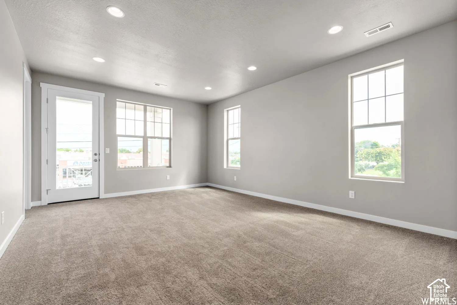 Neutral interior space featuring recessed lighting, wall-to-wall carpeting, multiple grid-pattern windows, and a glass-paneled exterior door