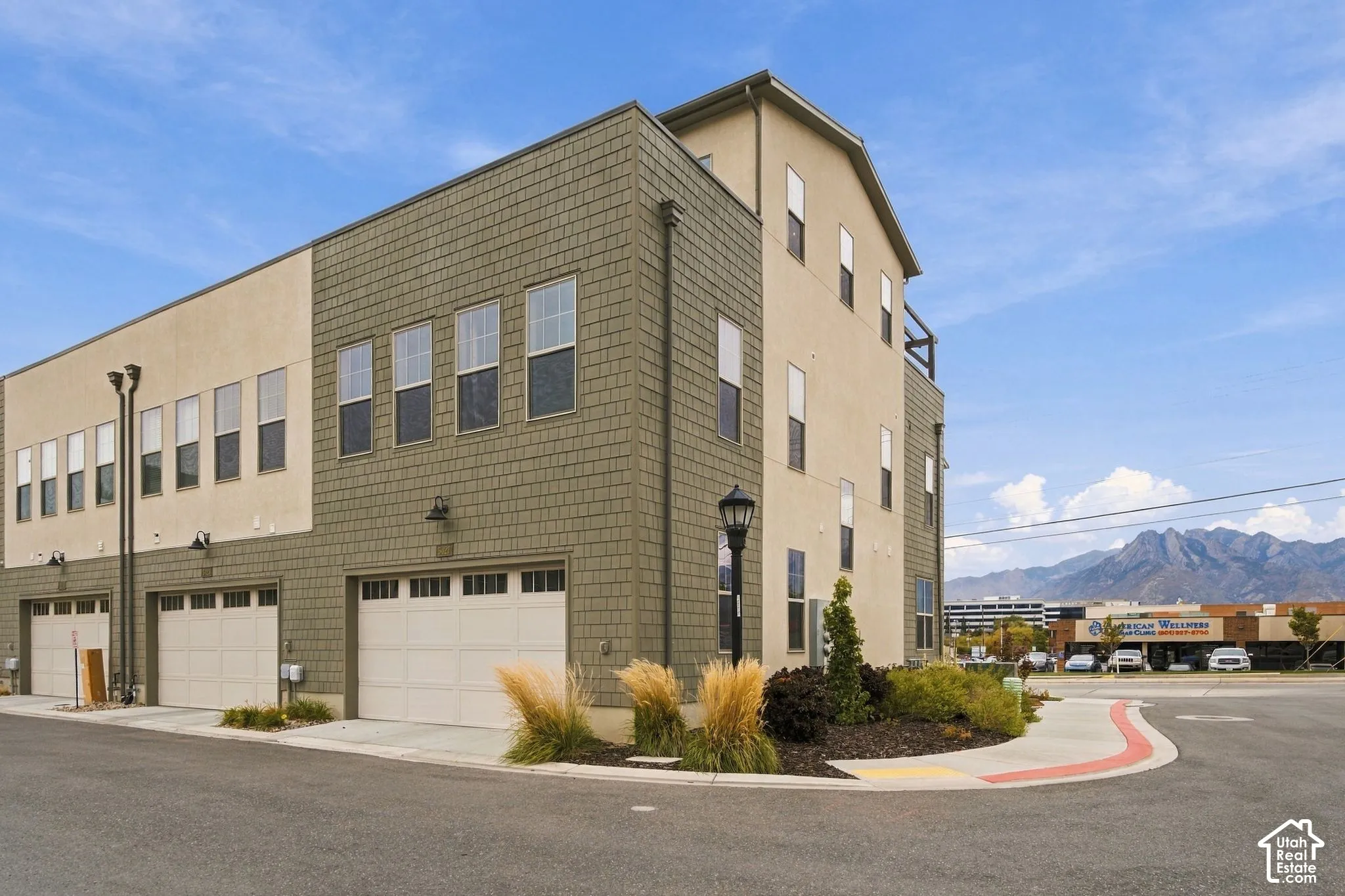 Three-story exterior featuring a mix of stucco and shake siding, multiple attached garages, and exterior wall-mounted lighting fixtures