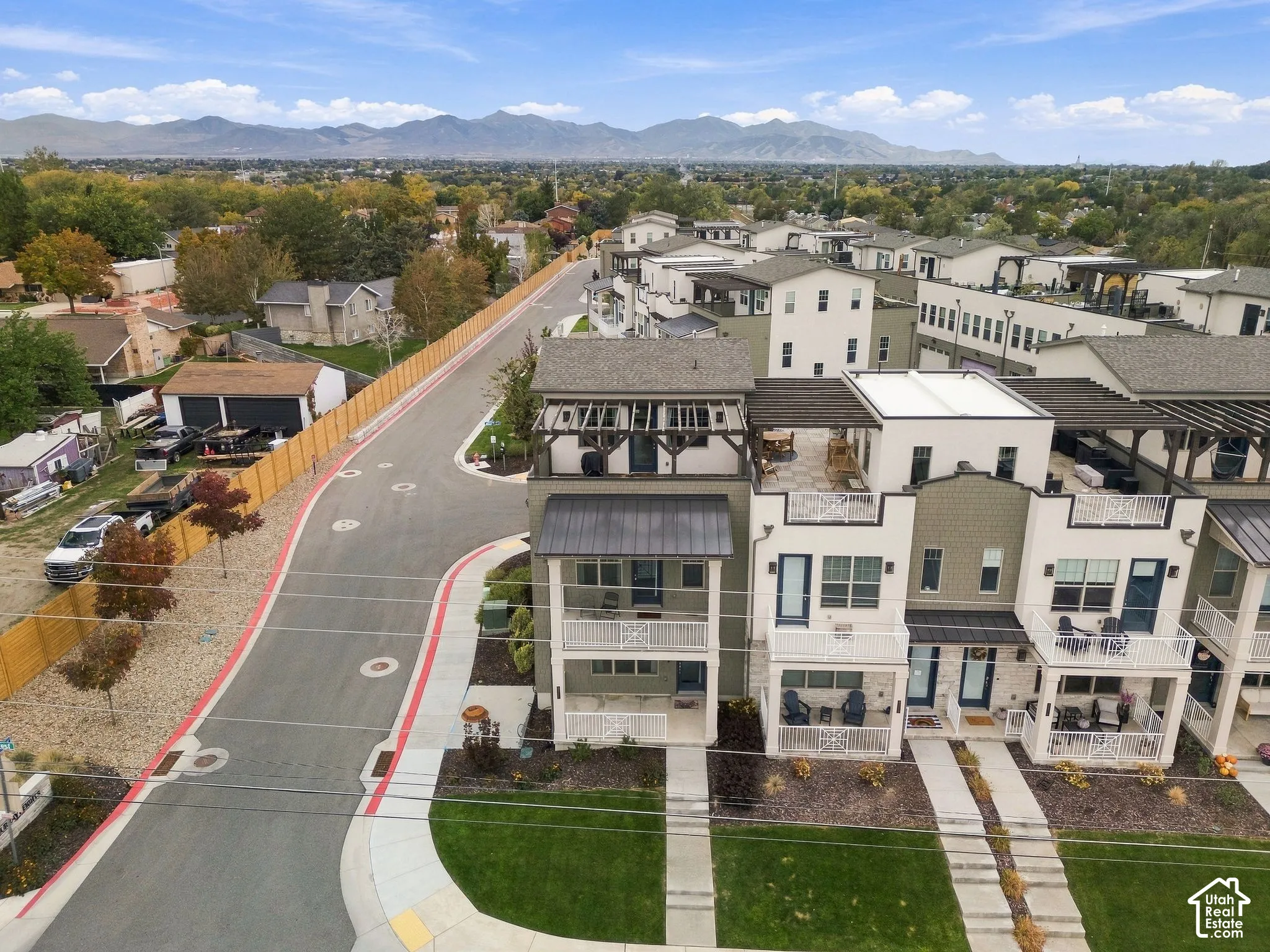 Multi-story townhome exterior featuring metal roof accents, upper-level private rooftop decks, attached balconies, and a mountain range backdrop
