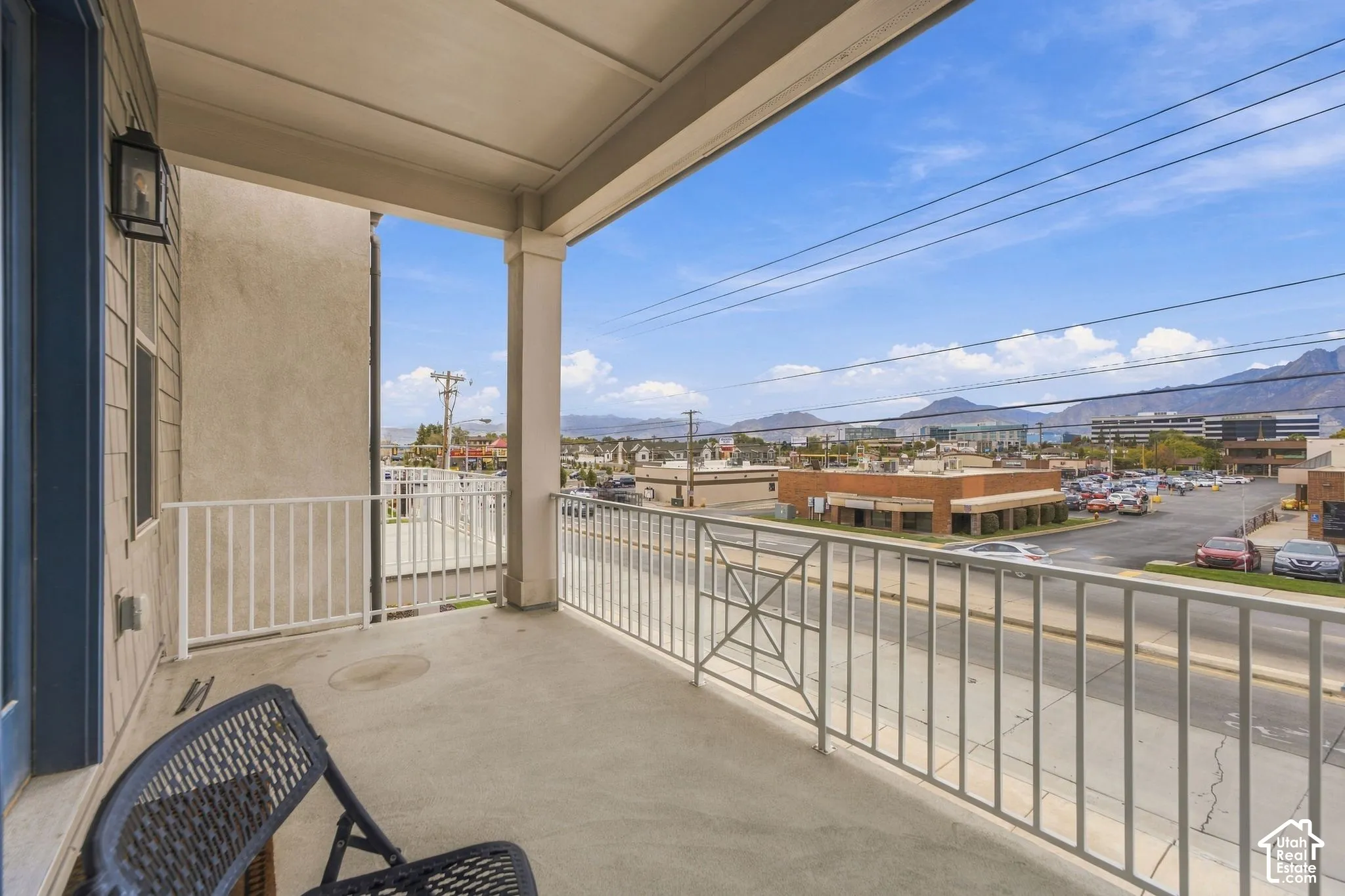 Covered balcony featuring concrete flooring, white metal railing, attached wall-mounted lantern-style lighting, and mountain scenery