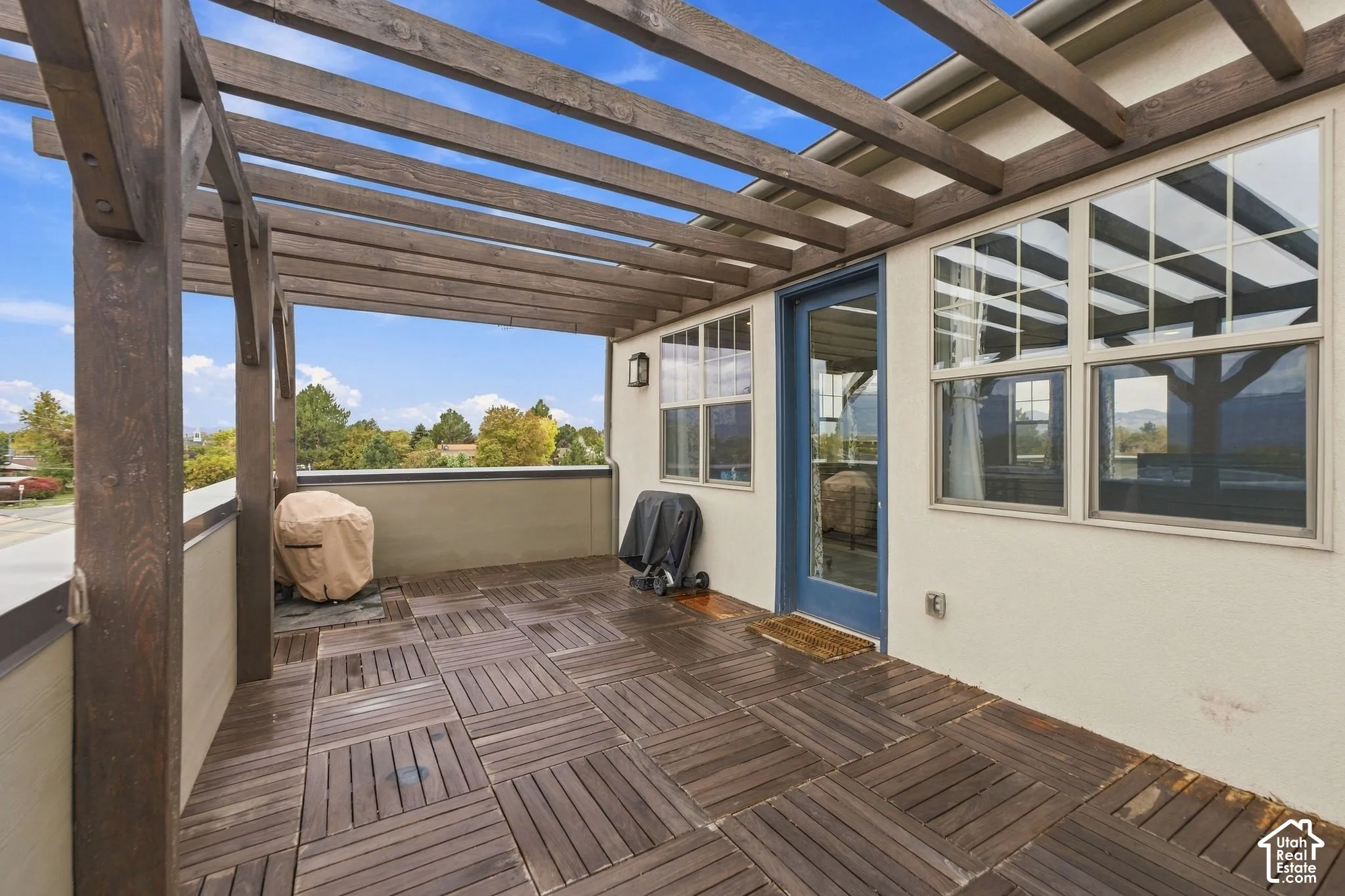 Outdoor terrace featuring a wooden pergola, modular wood-finish deck tiling, and a glass-paneled exterior door