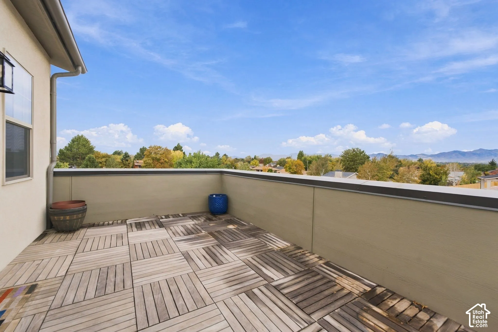 Open-air terrace featuring modular wood-finish deck tiles, solid perimeter walls with metal capping, and a mountain backdrop