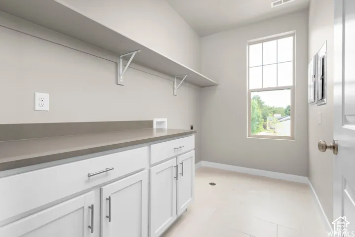 Utility space featuring white cabinetry with brushed-nickel hardware, neutral-toned solid surface countertops, a tall window, and tile flooring