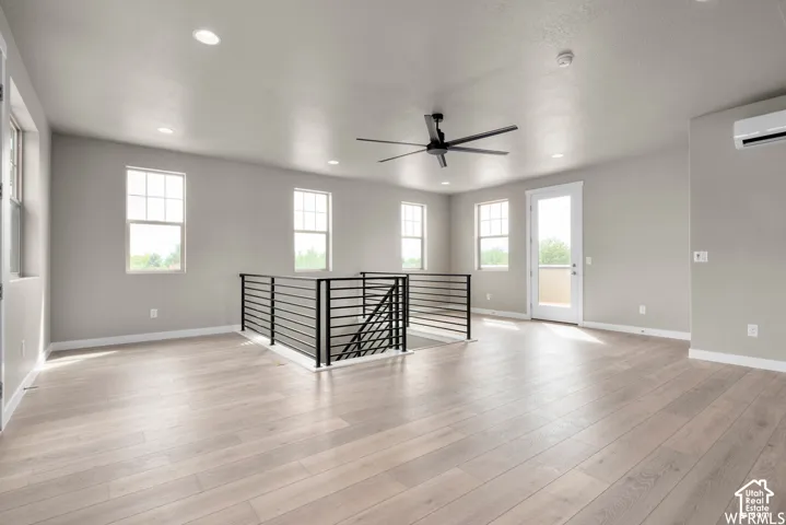 Open-concept space featuring wood-finish flooring, matte black metal railing, recessed lighting, a modern ceiling fan, and a wall-mounted climate control unit