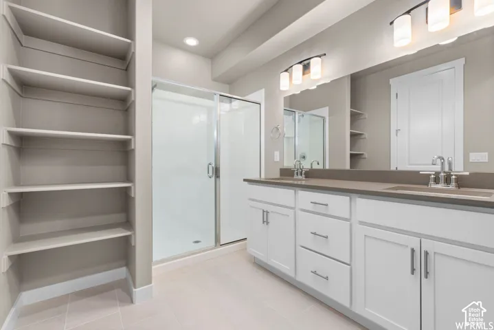 Dual-sink vanity with white cabinetry and solid-surface countertop, walk-in shower with glass enclosure, and built-in shelving unit
