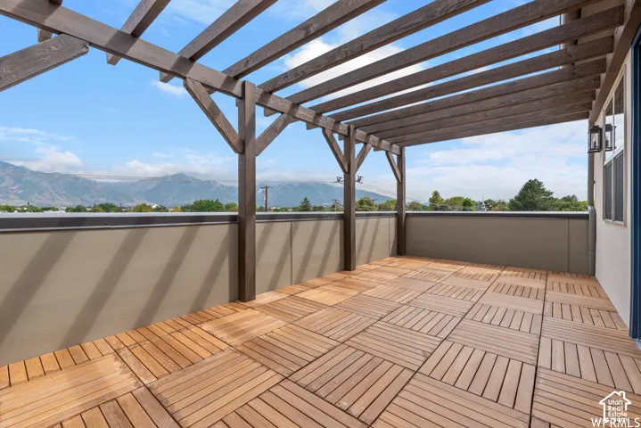 ORIGINAL PHOTOs Outdoor deck featuring a stained wood pergola, modular wood-finish flooring, solid perimeter walls, and a mountain backdrop