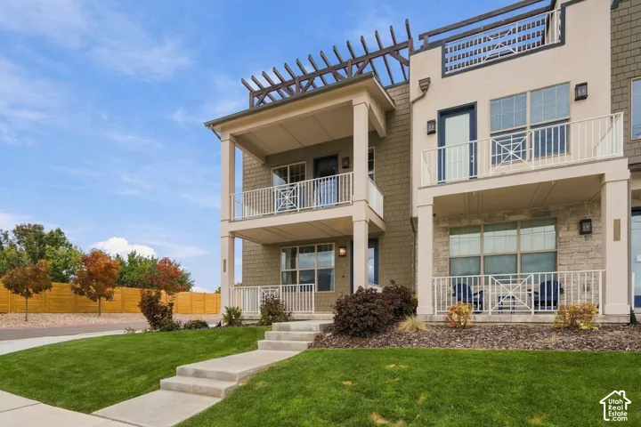 Multi-story townhouse exterior featuring shingle-style siding, stone veneer accents, multi-level balconies with white railings, and a rooftop pergola