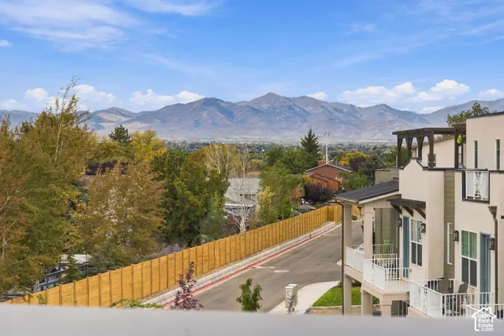 Multi-story exterior featuring a light-toned stucco and siding facade, private railed balconies, and a mountainous backdrop