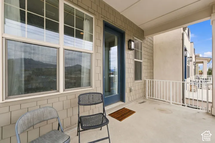 Covered balcony featuring shake-style siding, white metal railings, multi-pane windows, and a glass-paned entry door
