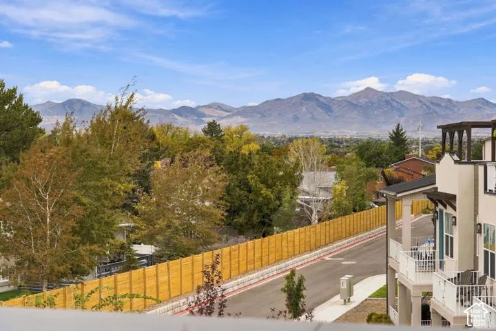 Stucco exterior building featuring multiple levels of balconies with white metal railings, a pergola-style roof structure, and mountain scenery