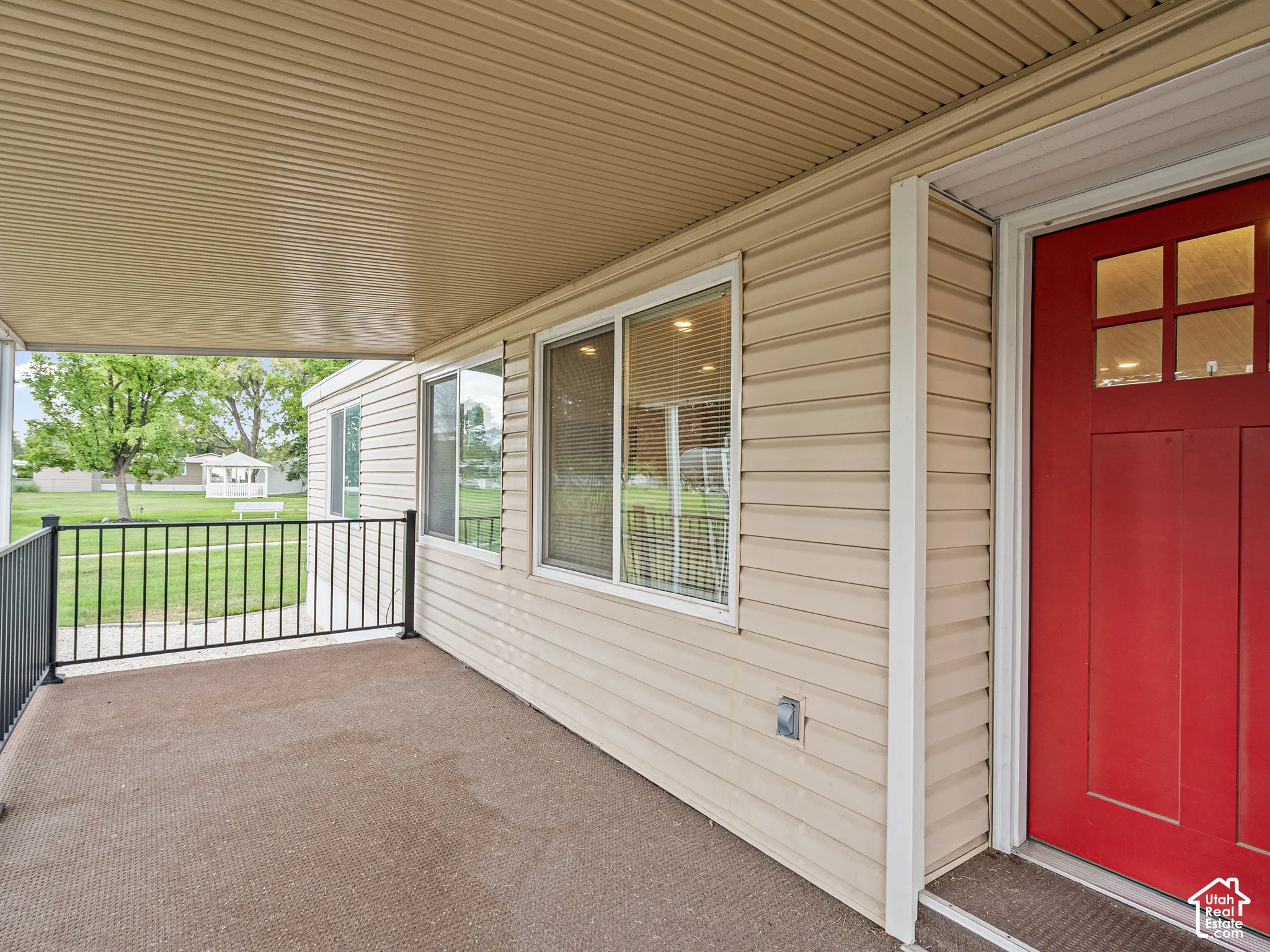 Covered porch featuring tan horizontal siding, a solid entry door with inset windows, and a black metal railing