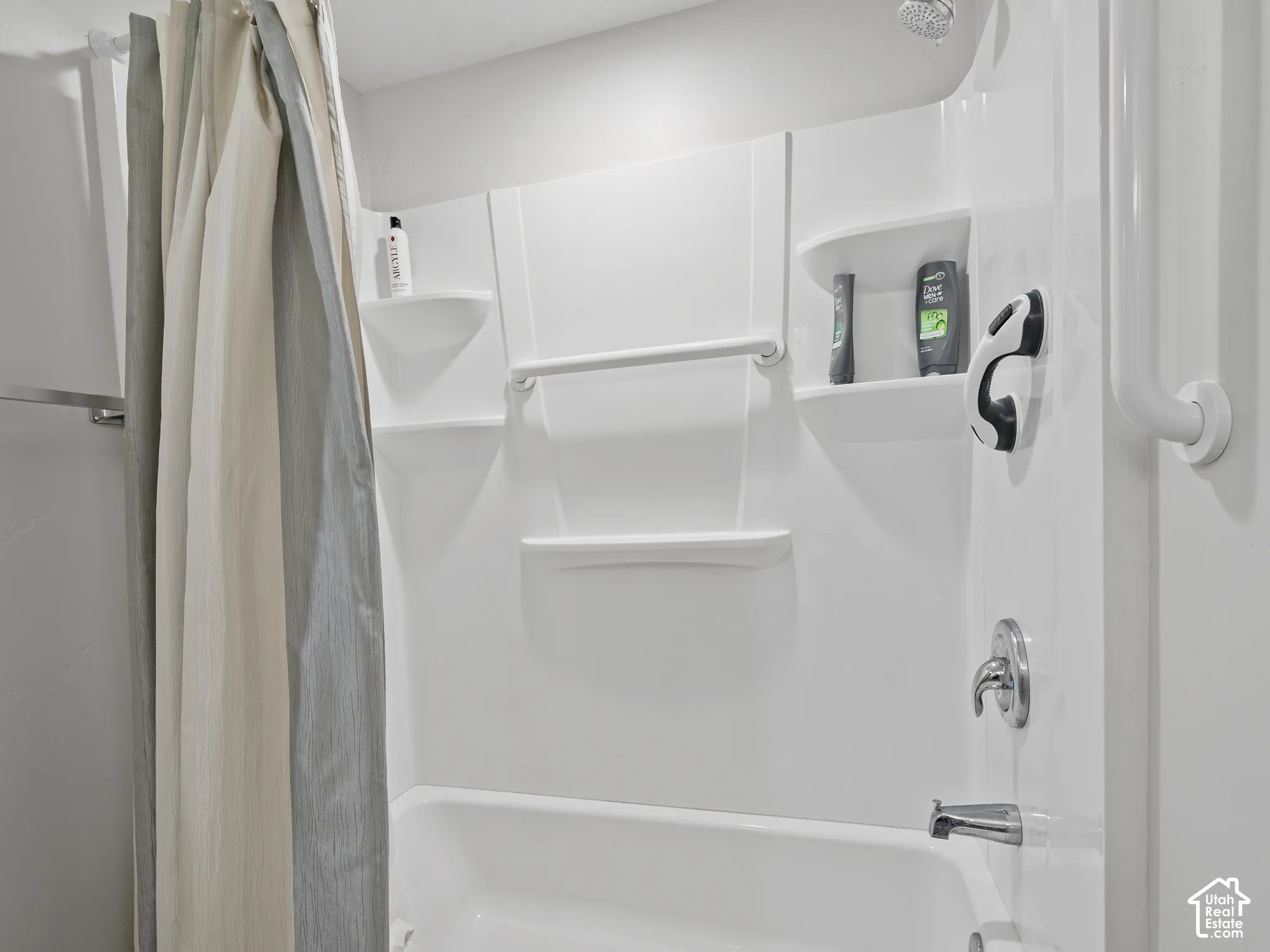Bathtub and shower combination featuring a white molded surround, integrated shelving, and a chrome single-handle faucet