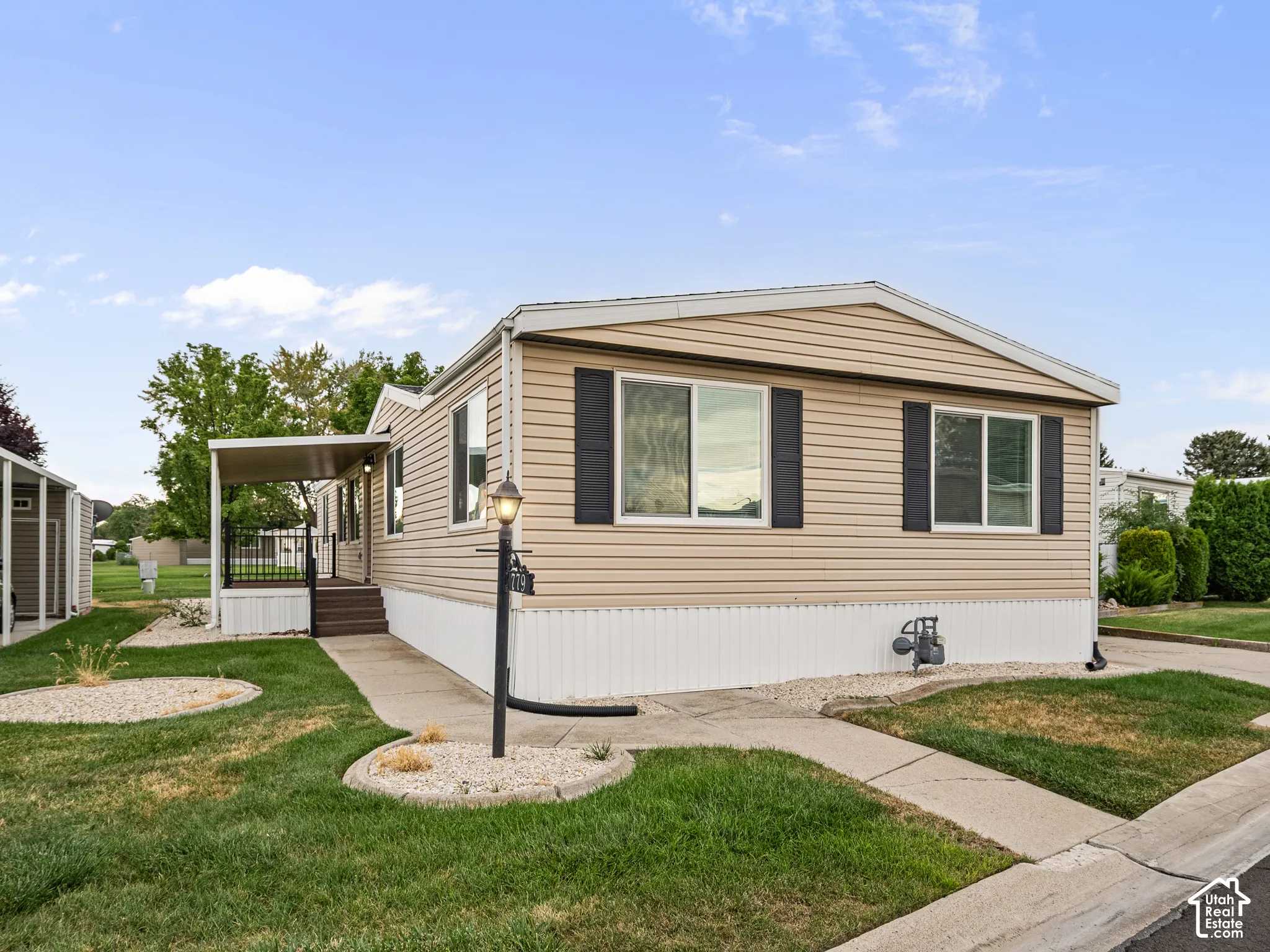 Exterior featuring light-tone horizontal siding, dark decorative shutters, a covered porch with metal railing, and concrete walkways