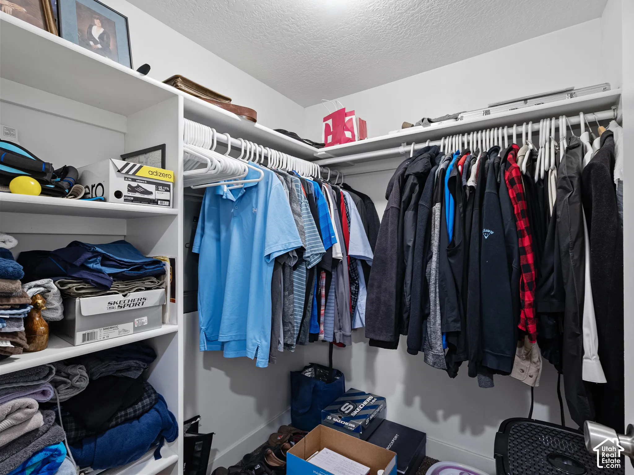Walk-in closet featuring white built-in shelving, white overhead hanging rods, and integrated wall-mounted electrical panel
