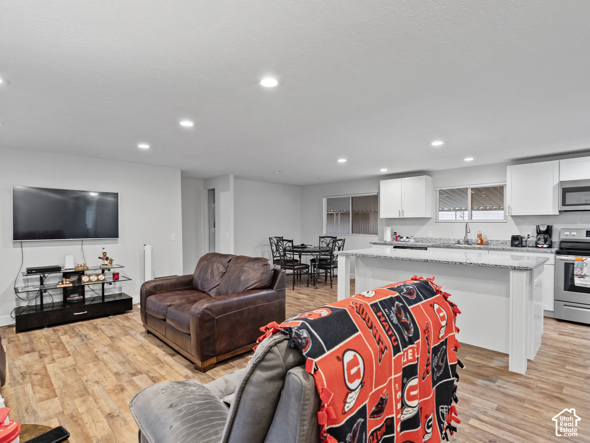 Open-concept interior featuring wood-finish flooring, recessed lighting, white cabinetry, a kitchen island with stone-finish countertops, and stainless steel appliances