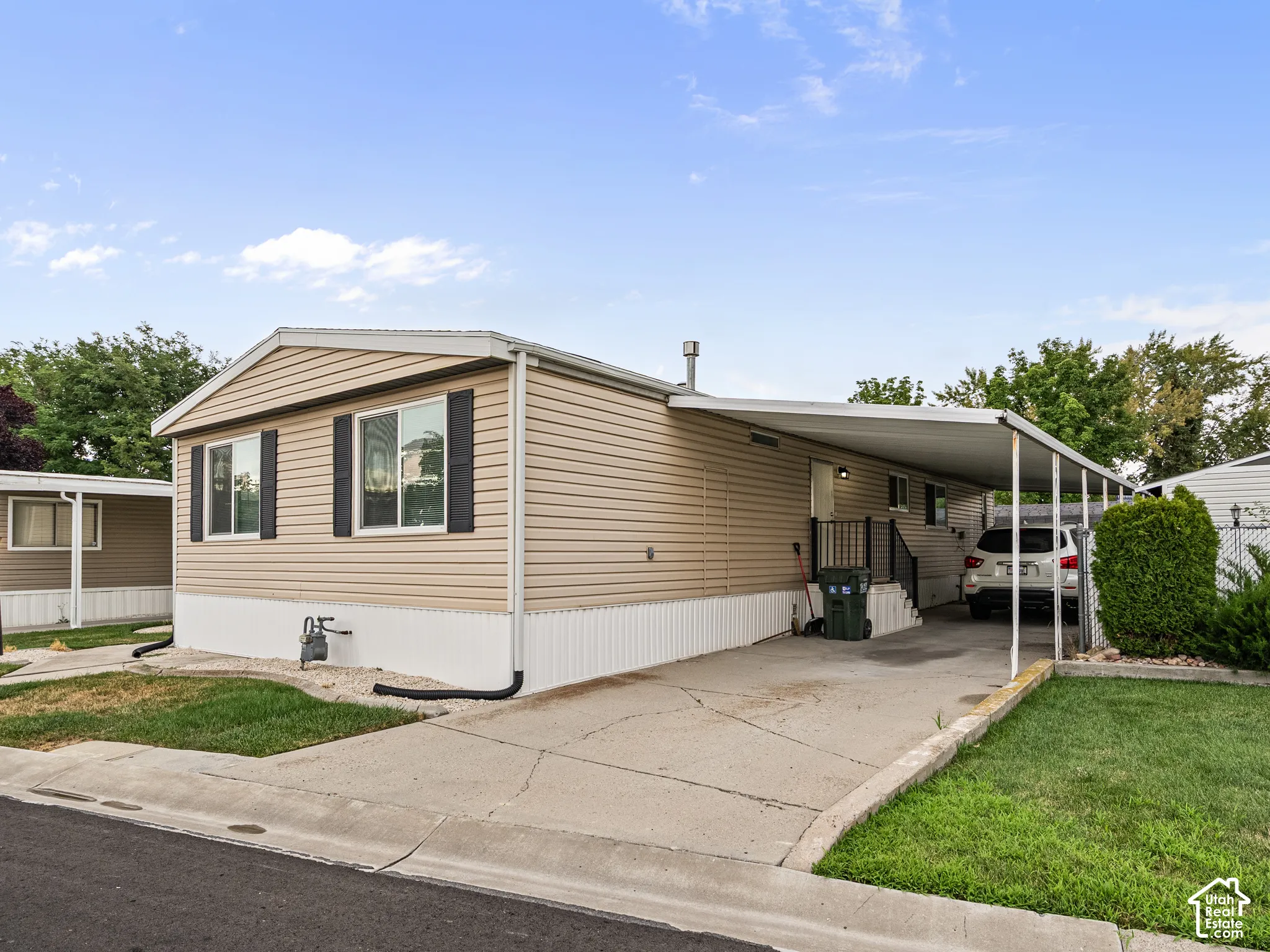 Exterior featuring tan horizontal siding, contrasting window shutters, concrete driveway, and covered carport