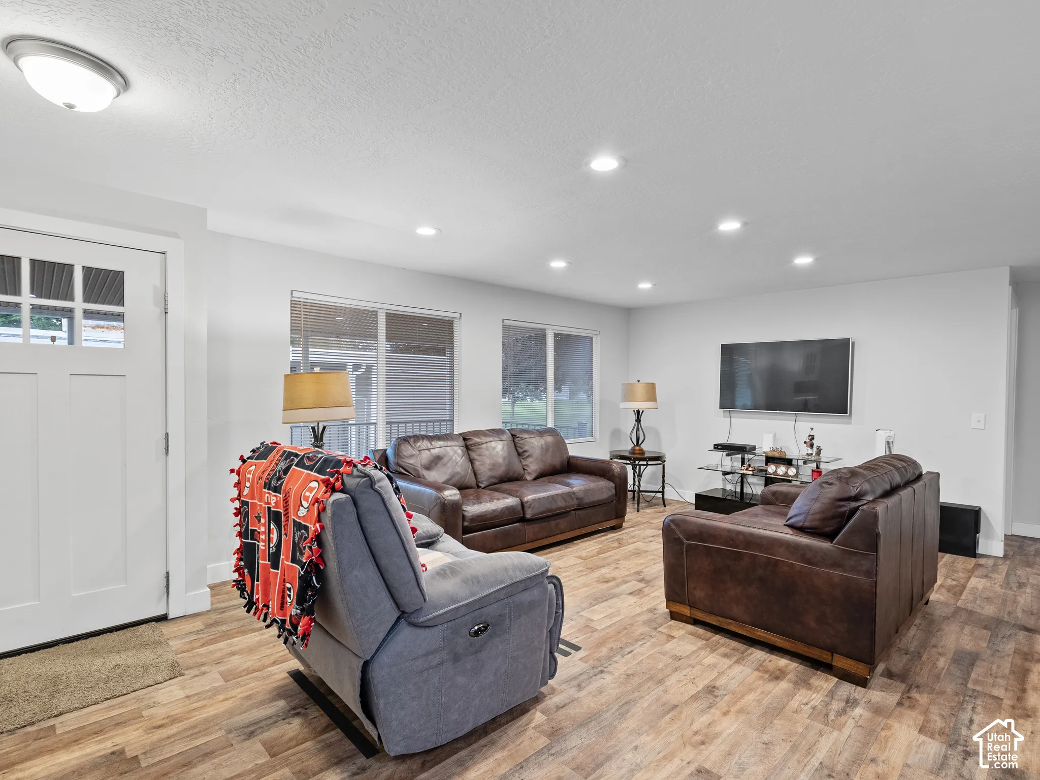 Open-concept interior featuring wood-finish flooring, recessed lighting, and a white six-panel exterior door with glass detailing