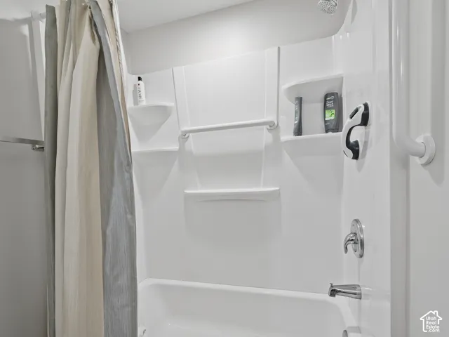 Bathtub and shower combination featuring a white molded surround, integrated shelving, and a chrome single-handle faucet