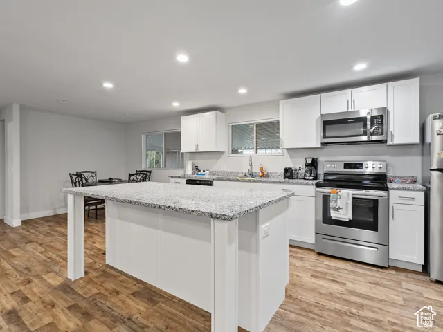 Kitchen featuring white shaker-style cabinetry, stone-finish countertops, a center island, stainless steel appliances, and wood-finish flooring