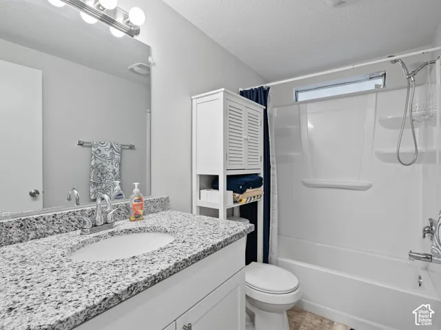 Bathroom featuring a vanity with a stone-finish countertop, undermount sink, multi-bulb wall-mounted lighting, and a combination tub and shower with a transom window