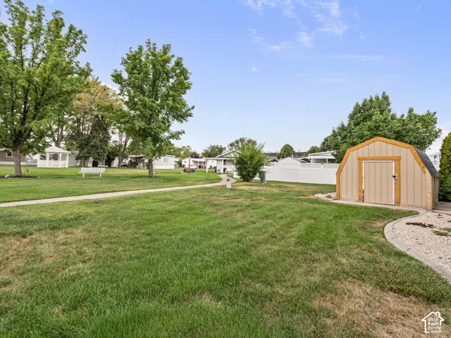 Expansive yard featuring a manicured lawn, detached storage shed, white vinyl perimeter fencing, concrete walkway, and mature trees