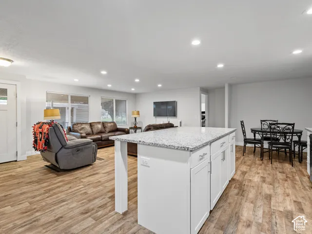 Open-concept space featuring wood-finish flooring, a kitchen island with stone-composite countertop, white cabinetry with silver-tone hardware, and recessed lighting throughout