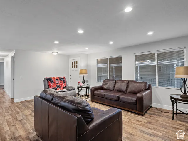 Living area featuring recessed ceiling lighting, wood-finish flooring, and large windows with horizontal blinds